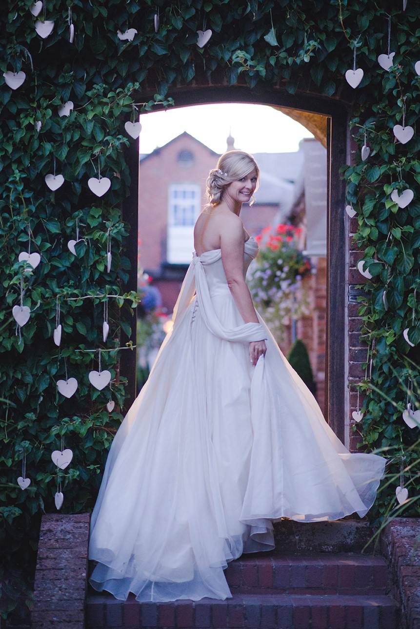 Bride in doorway to shambles with hanging hearts in ivy